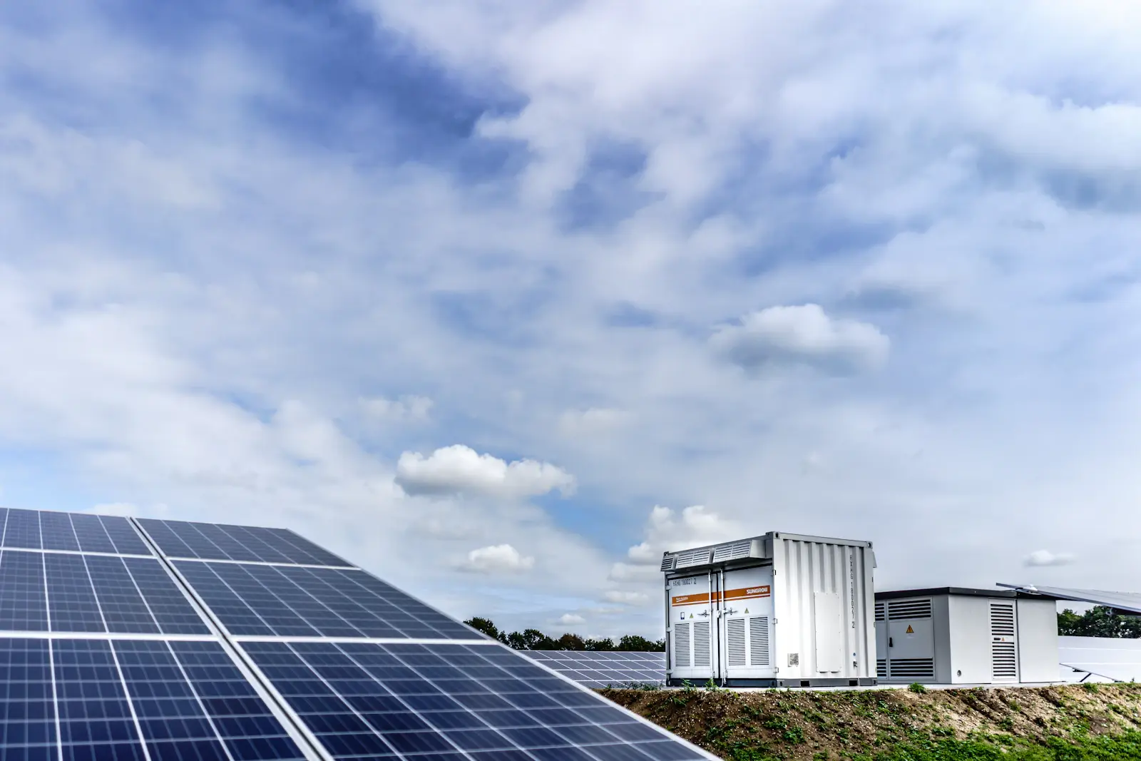 Contêiner de baterias (BESS) instalado ao lado de painéis solares, sob céu parcialmente nublado